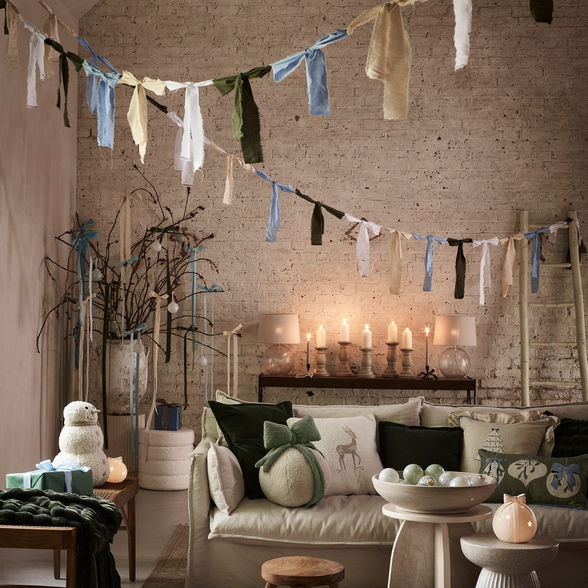 Exposed brick living room with green sofa and green festive cushions. There is bow bunting, candles and cream furniture.