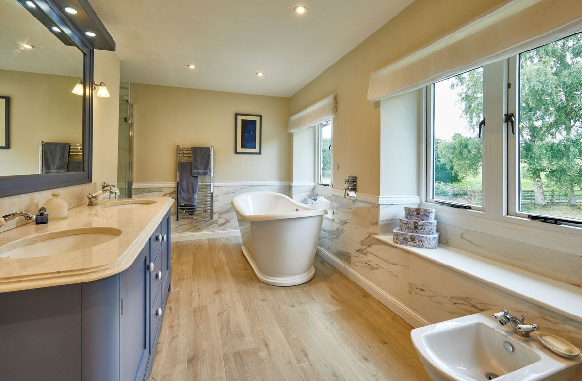 Bathroom with underfloor heating and a bath sitting next to the windows and opposite the sink with a walk in shower in the corner