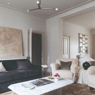 An off white-painted living room with a black velvet sofa and a marble coffee table