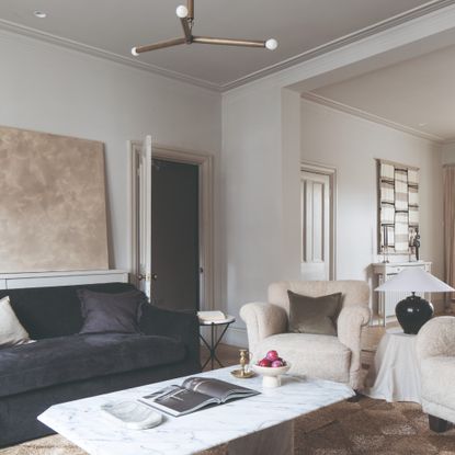 An off white-painted living room with a black velvet sofa and a marble coffee table