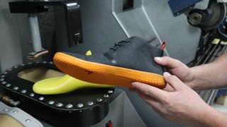 Person holding a Vivobarefoot shoe in their hand in a factory