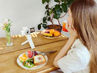 A person vlogging with the Sony ZV-1F placed on a table surrounded by food