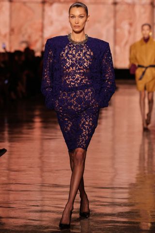 Bella Hadid walks the Saint Laurent Fall 2025 runway wearing a lace naked dress from the brand with black pumps and a slicked back bun