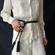A woman wearing a white set with a black tassel belt. 