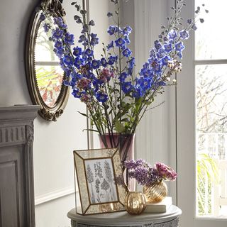 round mirror on wall flower in vase and white window
