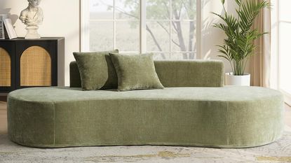 Image of a velvet, sage green curved sofa with two matching pillows on it.