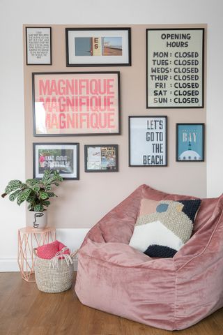 Corner of an open-plan room with a pink velvet beanbag chair, pink painted square on the wall filled with prints to create a gallery wall
