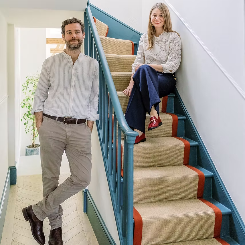 male and female in hallway with blue painted stairs with sisal runner with red border