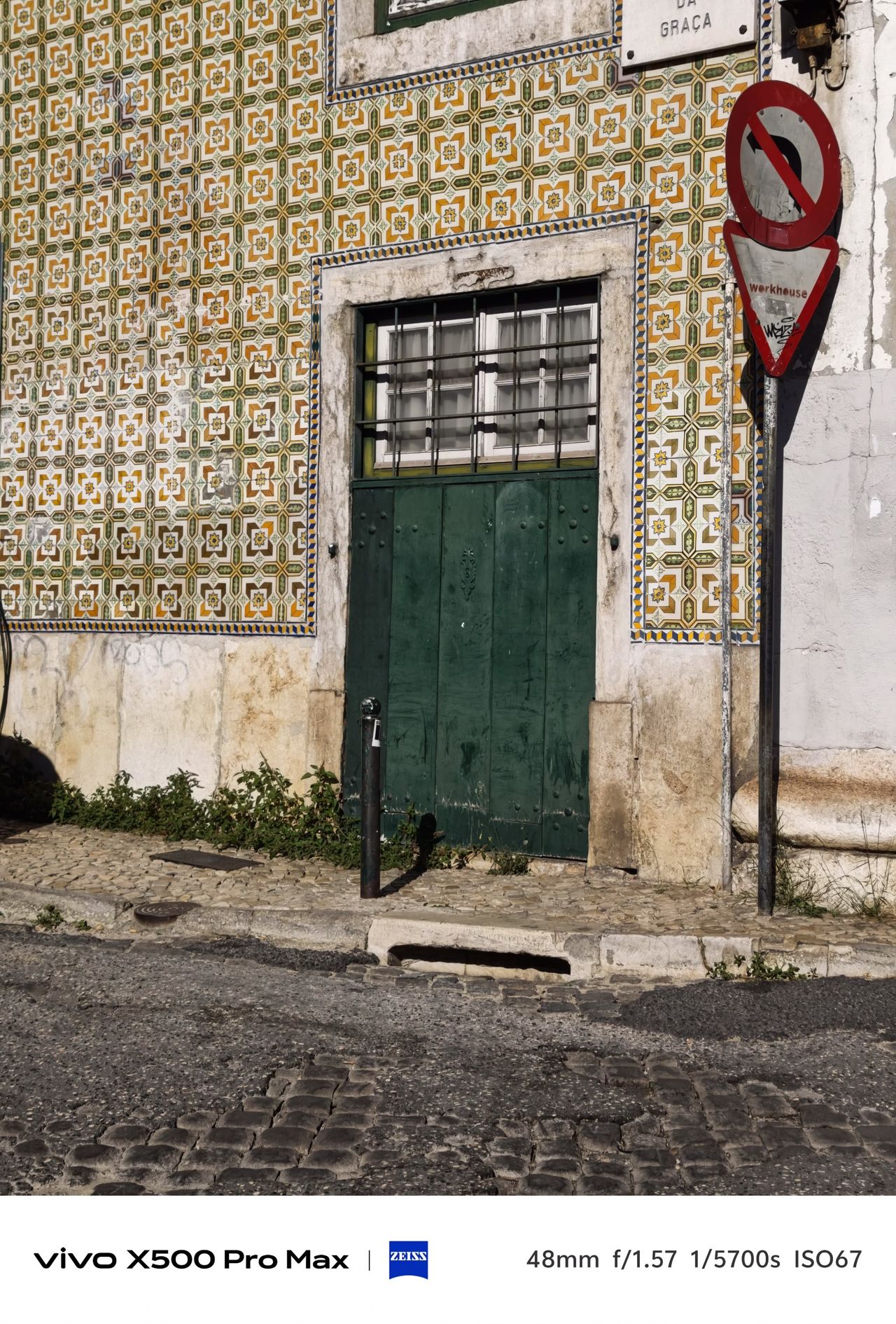 Green wooden door surrounded by patterned Portuguese tiles on a sunlit facade.