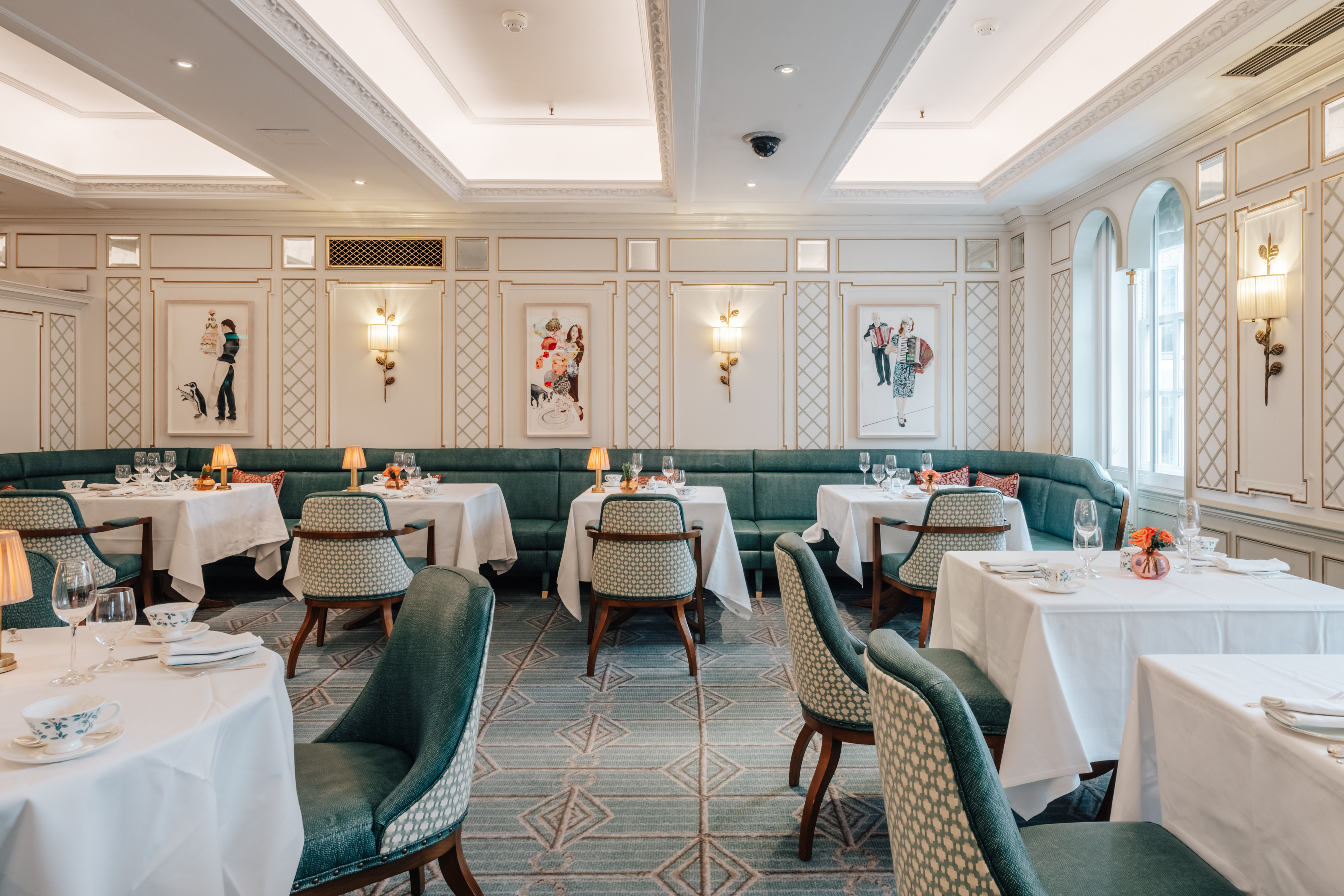 An Art Deco-infused tea room with plush, teal seating, spirited artwork, golden lighting, and textural table lamps.
