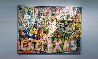 A large piece of artwork on display with multi-coloured drawings and the word ERZTEXAS drawn in red at the bottom.
