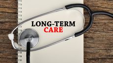 The words long-term care on an open notebook with a stethoscope wrapped around them.