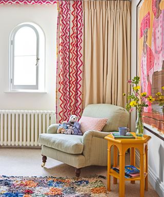 cream girl's bedroom with red patterned curtains, neutral armchair, patterned rug and statement artwork