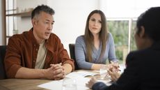 A couple talk with a financial adviser while sitting at their dining table in their house.