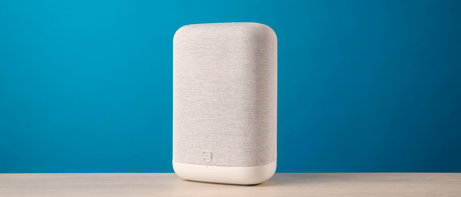 the bluesound pulse flex wi-fi speaker in pale gray photographed against the blue tom's guide background