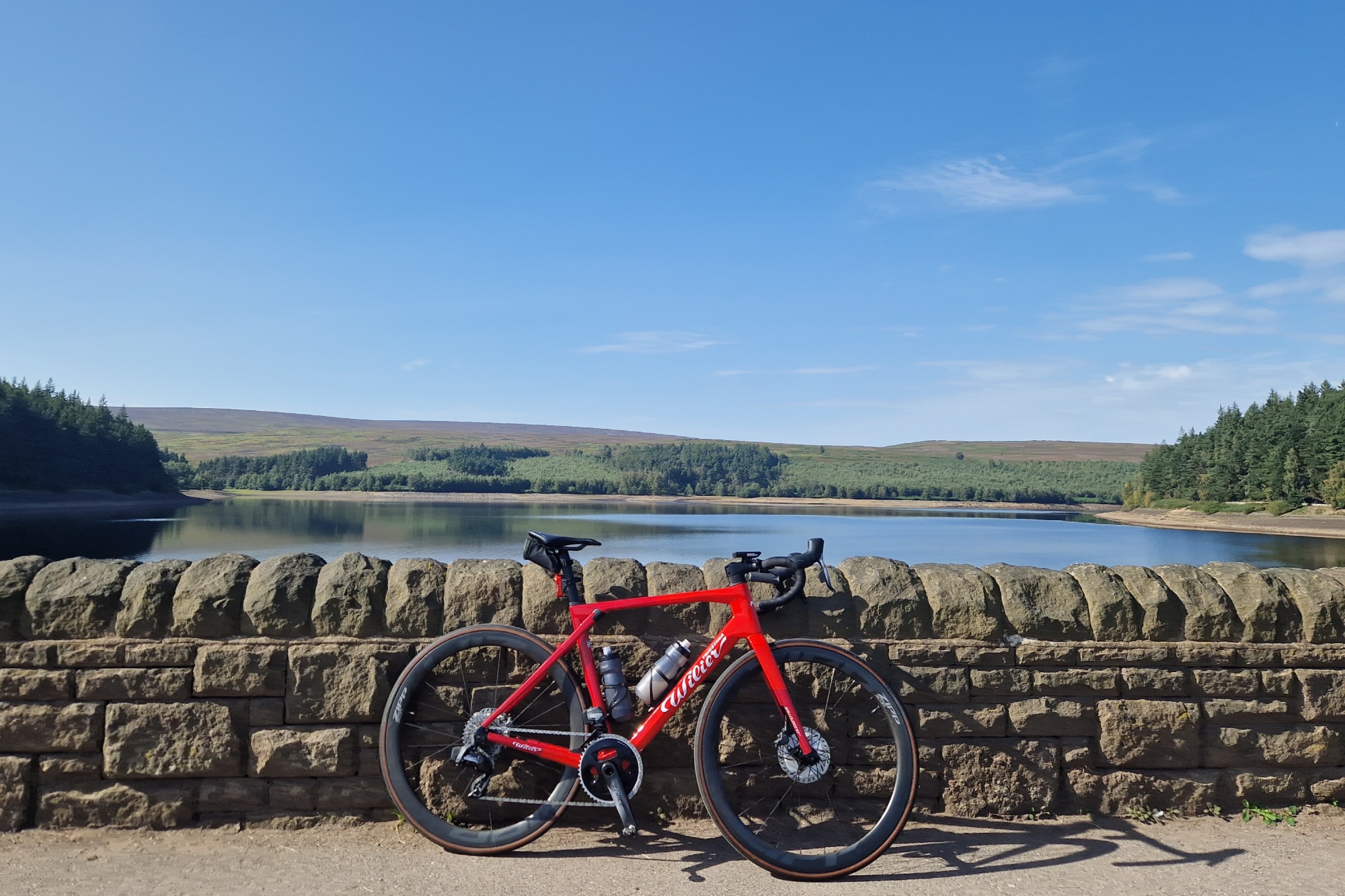 The Wilier Granturismo SLR leaning against a stone wall in front of a reservoir with hills and blue sky in the background