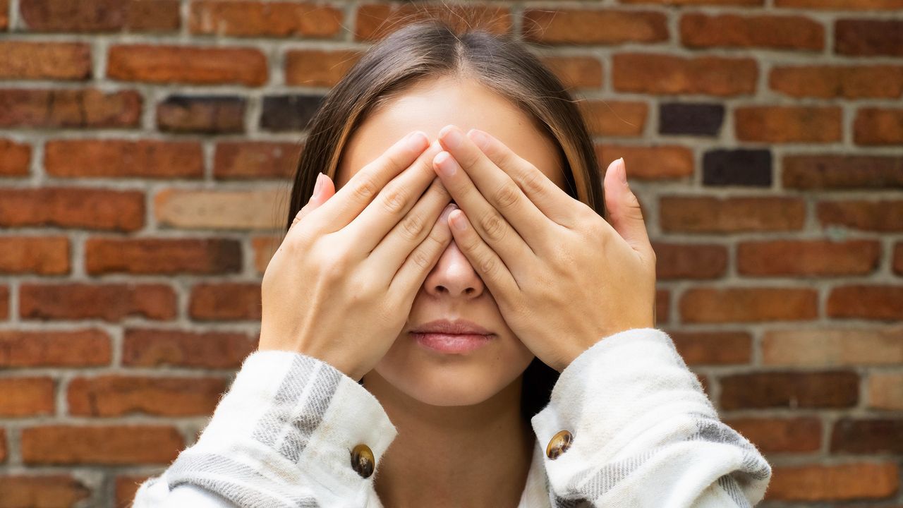 A young woman covers her eyes.