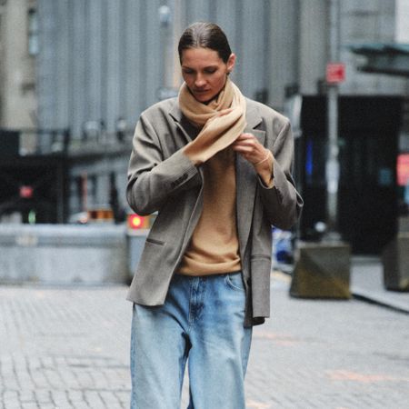 A Zara model shot on the street wearing a grey blazer and camel-colored sweater with jeans