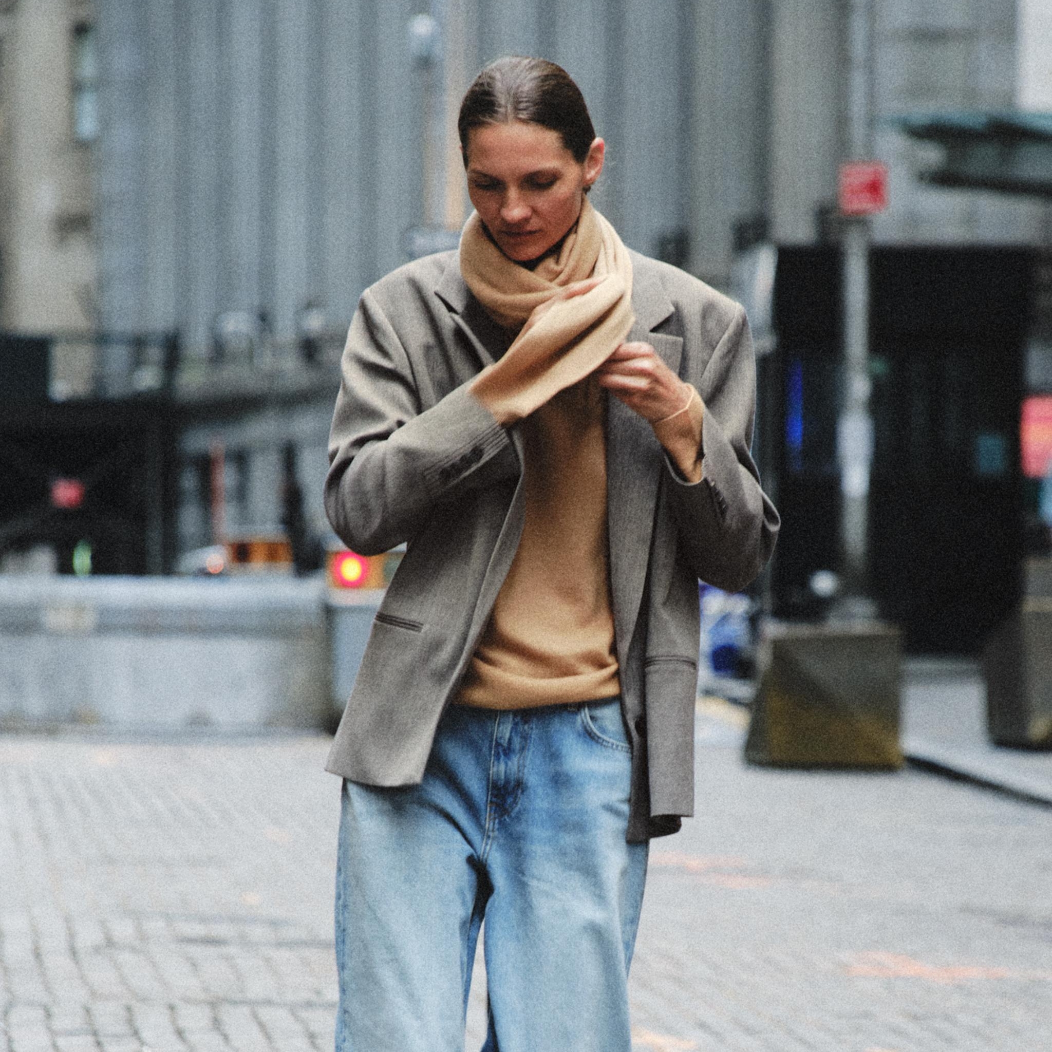 A Zara model shot on the street wearing a grey blazer and camel-colored sweater with jeans