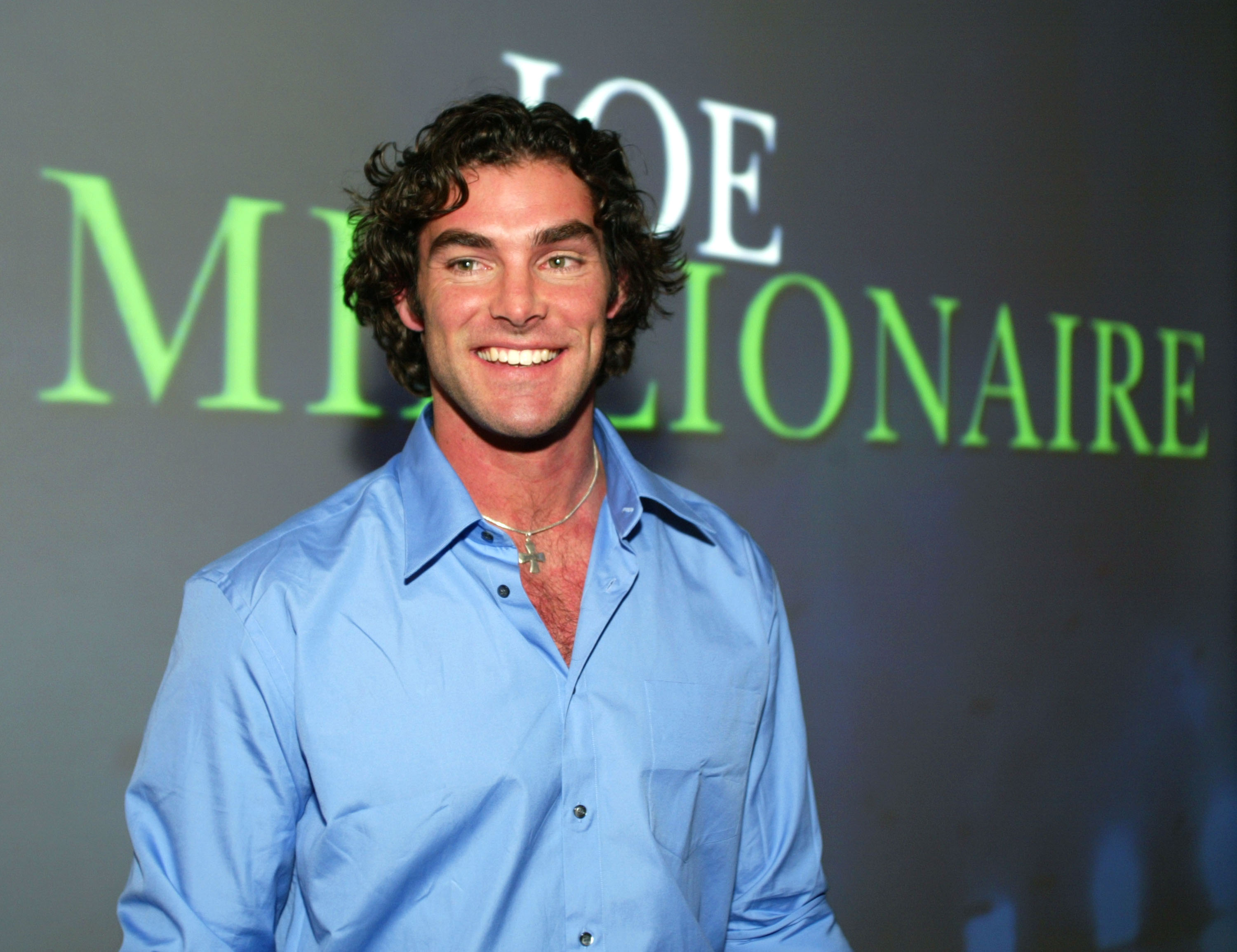 a man in a blue shirt stands on a red carpet promoting the show Joe Millionaire