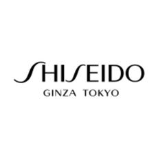 Photo of Shiseido day cream with gold and purple bottle on pale pink background with two single orange flowers