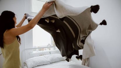 A woman airing her duvet over her bed