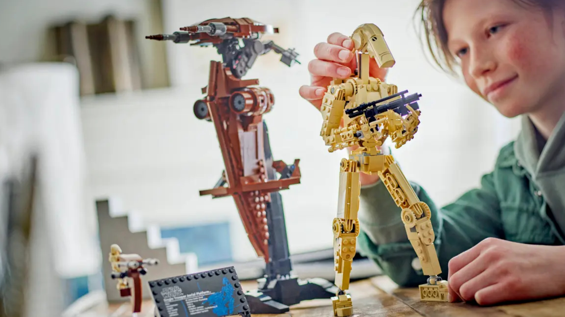A child poses the Lego Battle Droid on a wooden table