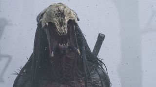 The Predator, with its skull helmet on its head, roars on a barren, smoke-filled landscape in Prey