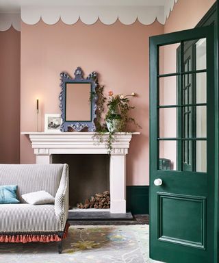 living room with pink walls, dark green doorway, gray striped sofa and mantel with mirror, candle, and potted plant