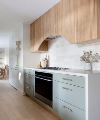 A blue, white, and wood galley kitchen with gold hardware and wood flooring