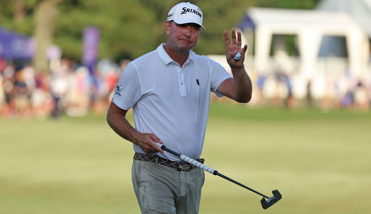 Lucas Glover raises his putter and waves to the crowd