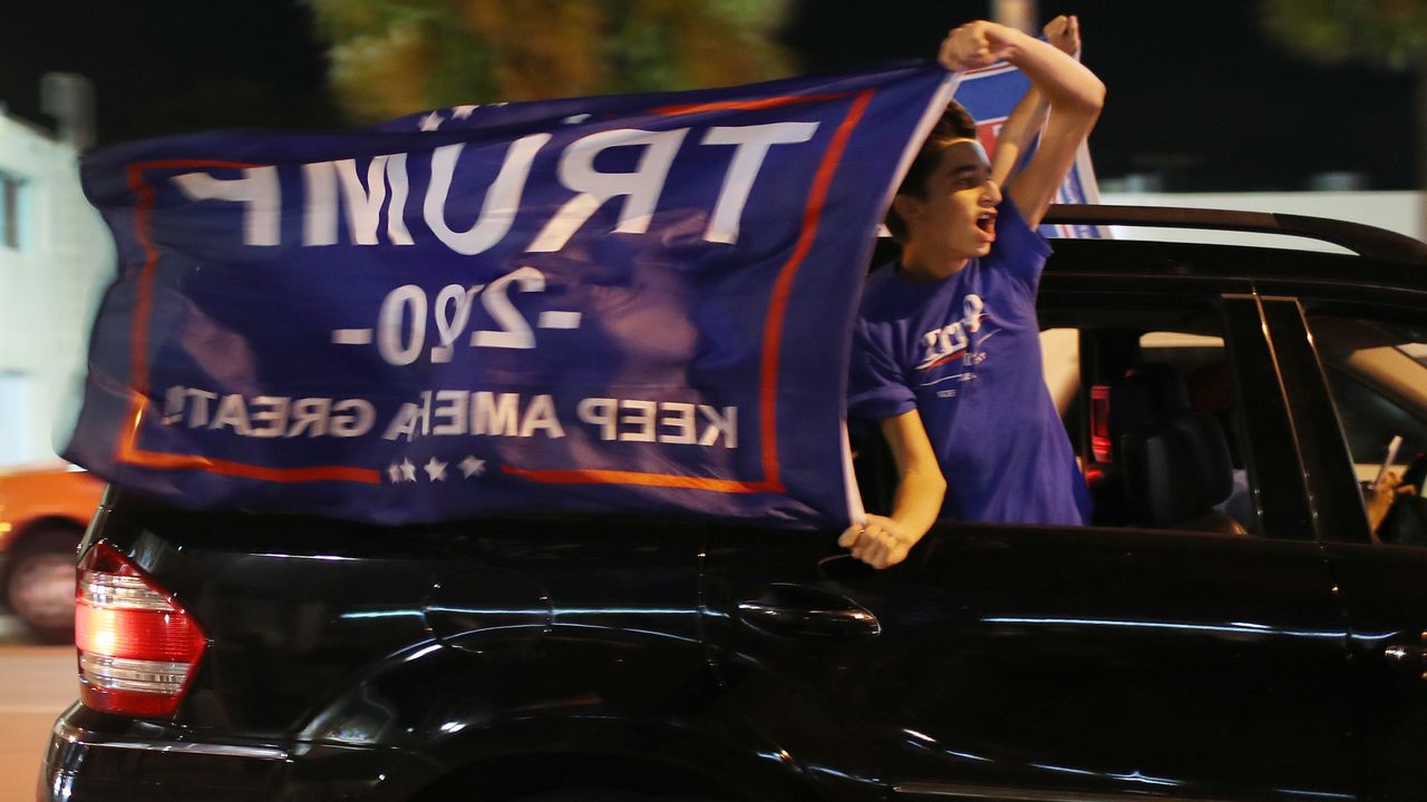 A Donald Trump supporter flies a &amp;quot;Keep America Great&amp;quot; flag out of the window of a moving car.