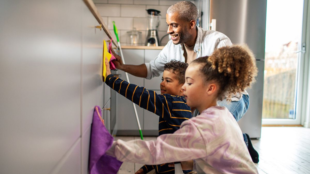 Two kids and their dad cleaning kitchen cabinets using colored microfiber cloths.