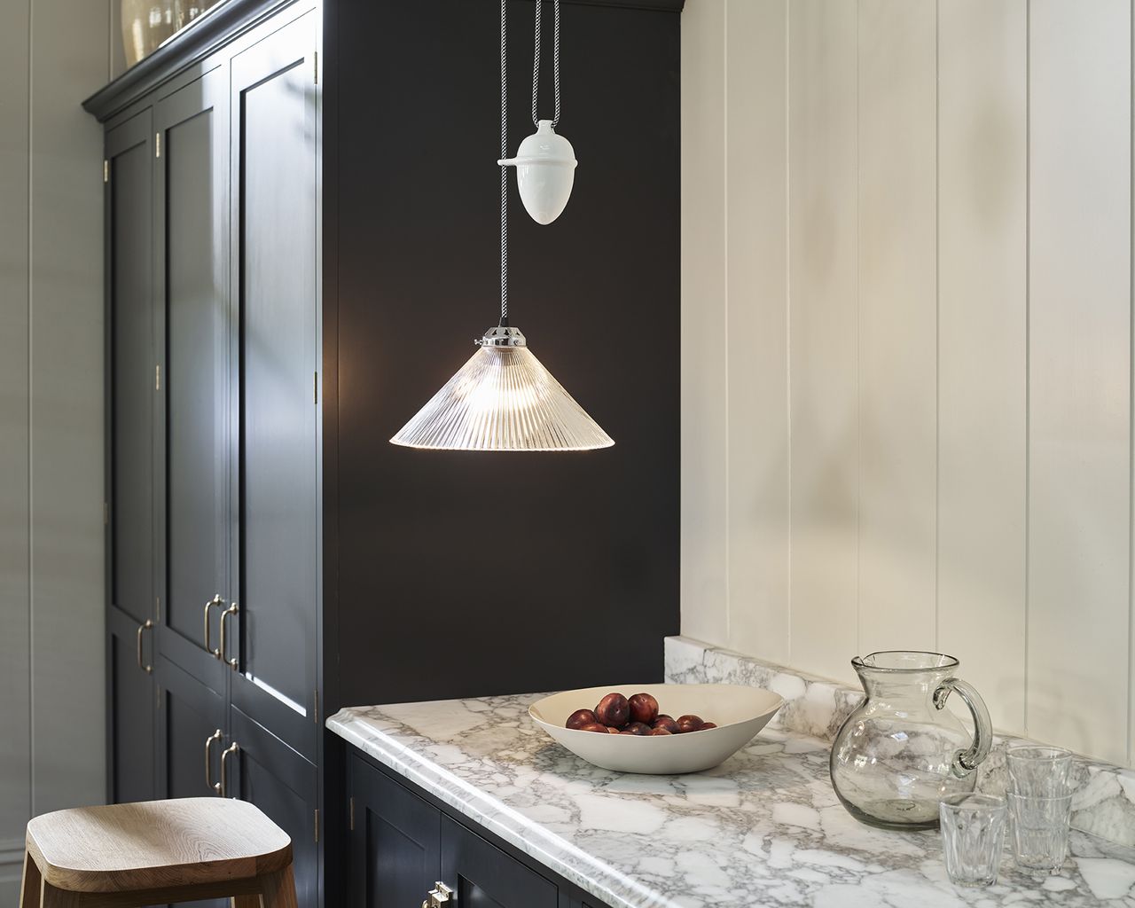 A conical prismatic glass pendant hanging over marble worktop in kitchen with adjacent black dresser