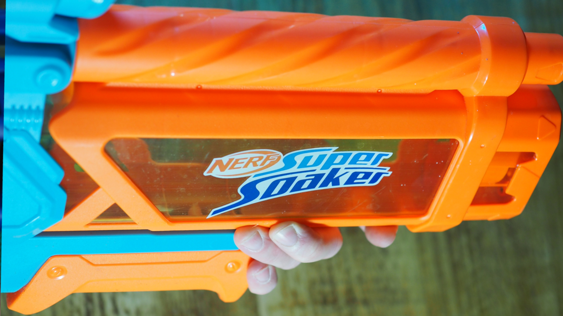 A hand holds a Super Soaker above a wooden surface