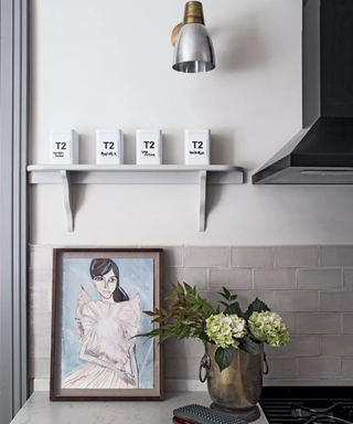 Downlighting as an example of kitchen wall lighting ideas in a small kitchen with gray tiles, a vase of flowers and a painting.