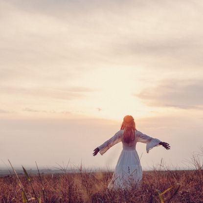 A woman, standing in a meadow at sunset