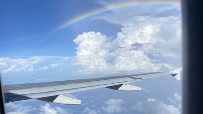 The view of a rainbow over some light clouds from an airplane window.