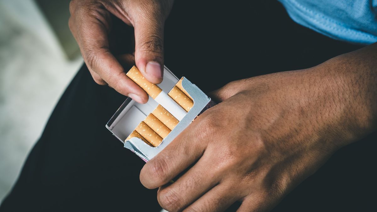 Close up of man&#039;s hand taking a cigarette out of a cigarette packet. 