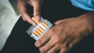 Close up of man's hand taking a cigarette out of a cigarette packet. 