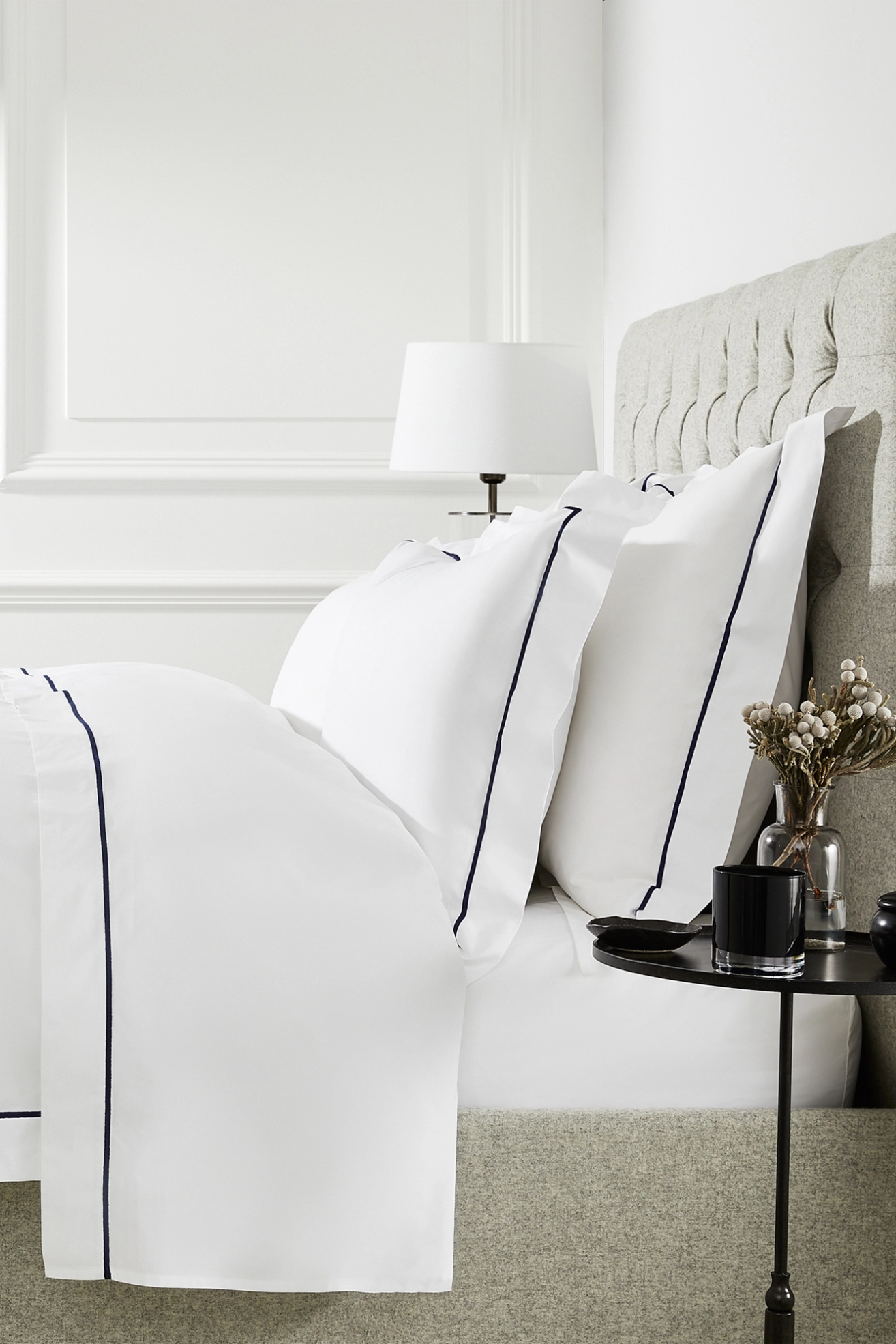 A bed with white sheets and black piping