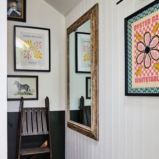 A small black and white-painted hallway with a gallery wall and a mirror hung on the wall