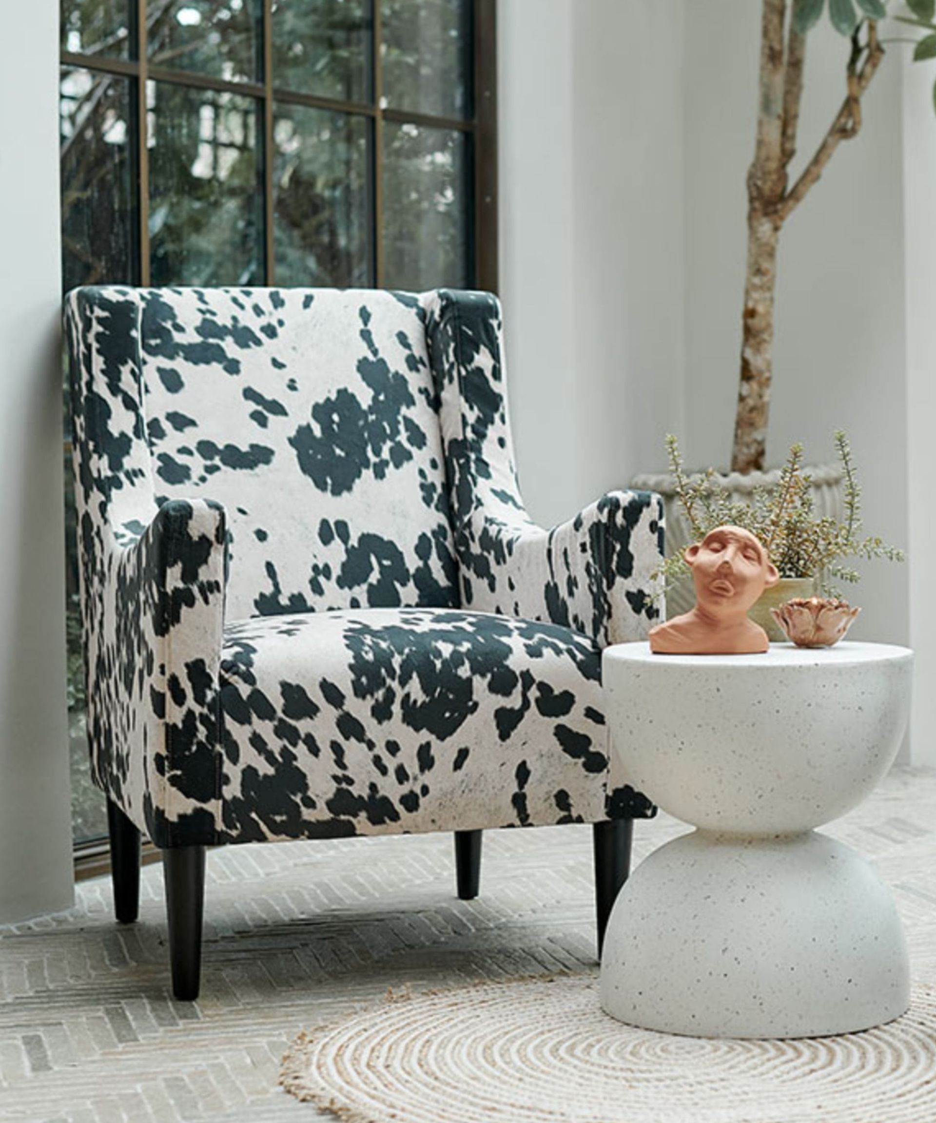 A bright white room with a black and white cow print armchair and a small white table