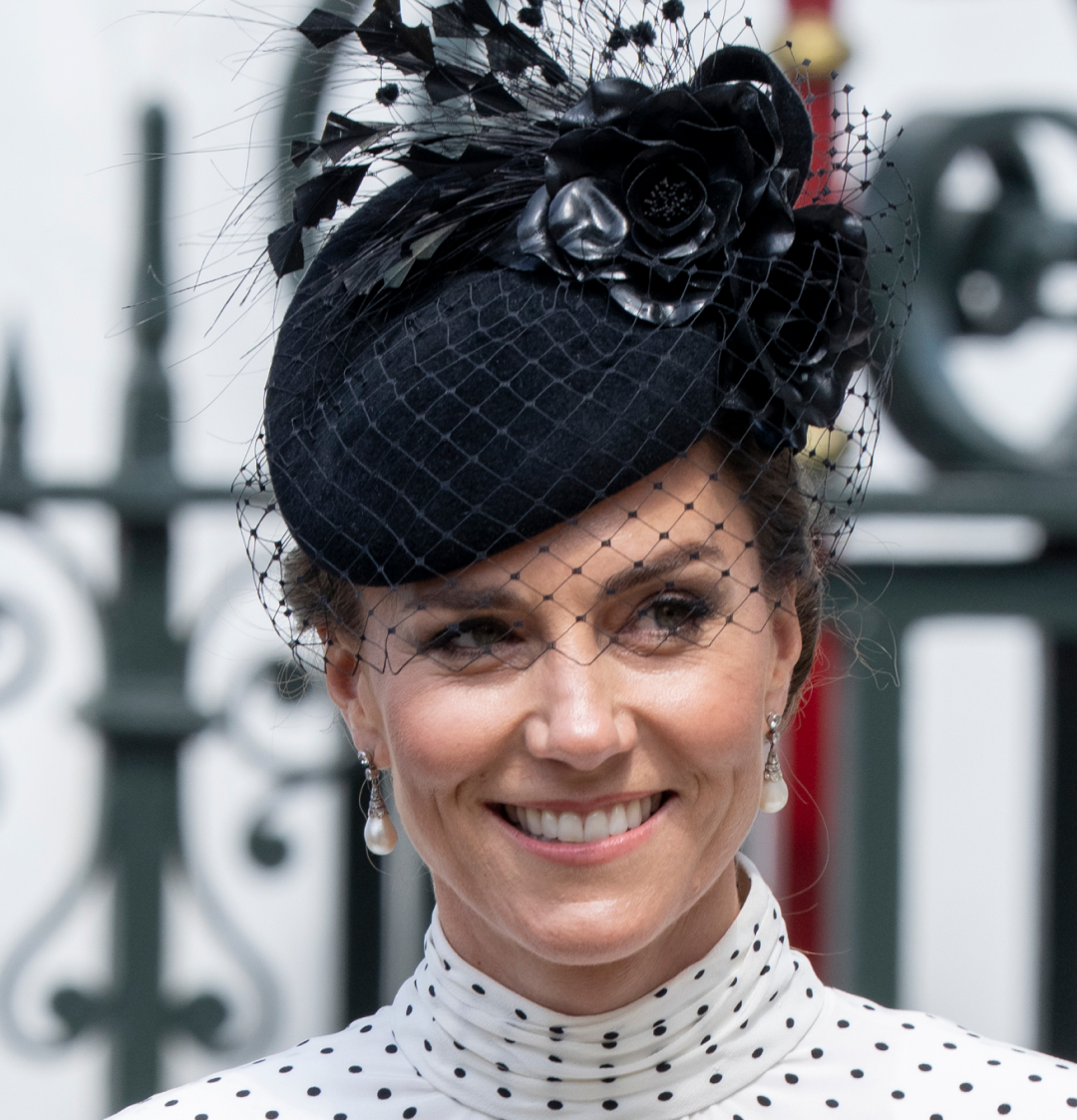 Kate Middleton wearing a white polka dot dress and black hat smiling