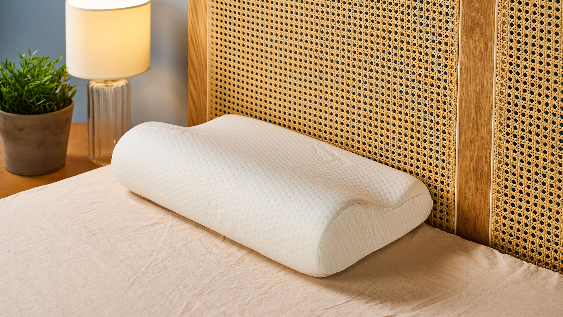 A white pillow placed on the bed next to a rattan headboard