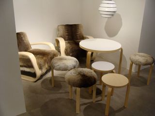 A Room with white walls featuring Upholstered chairs in swedish reindeer fur with matching side tables. White Beehive style hanging ceiling lights