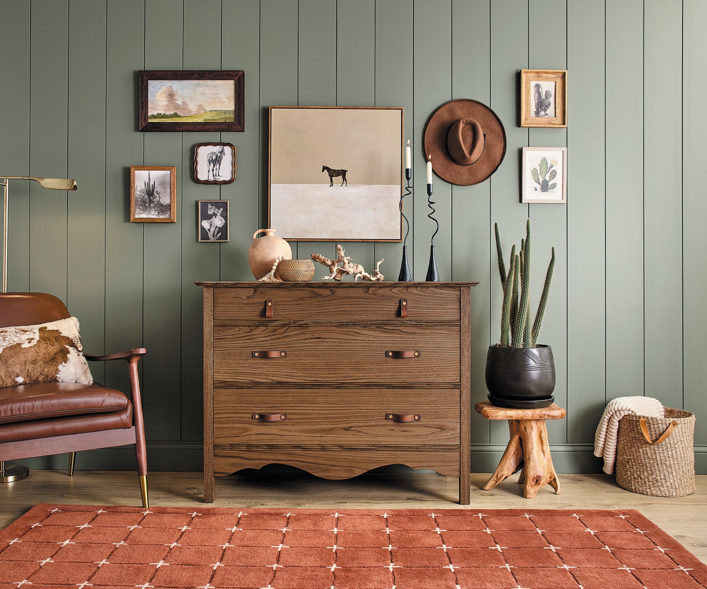 Paneled wall painted sage green, terracotta rug and walnut wood dresser with decor and gallery wall
