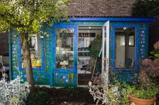 a shed painted blue with lots of decorative pattern and flowers, used as an art studio