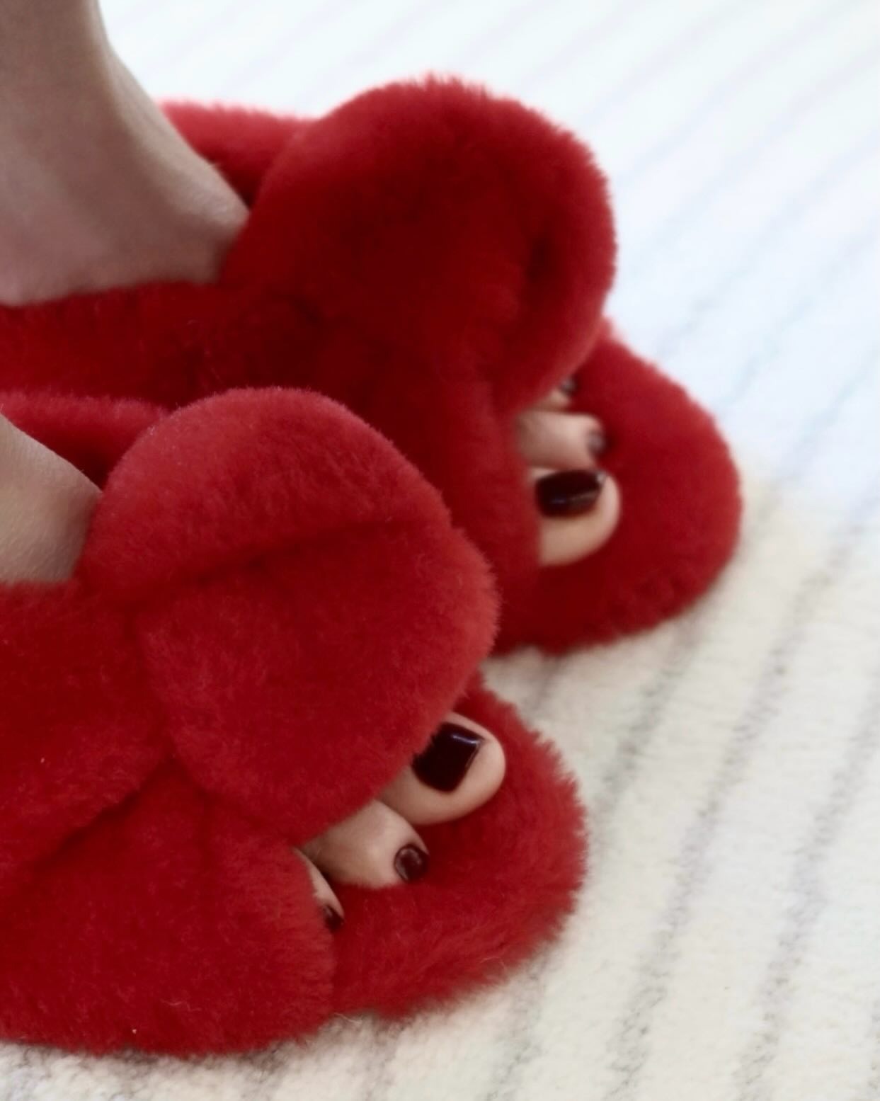 A woman wearing fluffy red shoes with a deep cherry pedicure