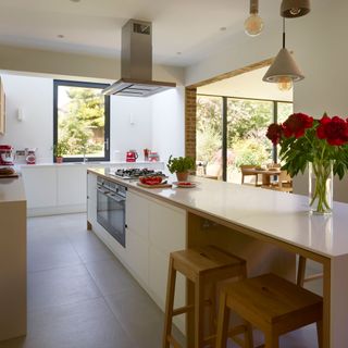 pale kitchen island with inbuilt oven and wooden stools, with overhead extractor fan